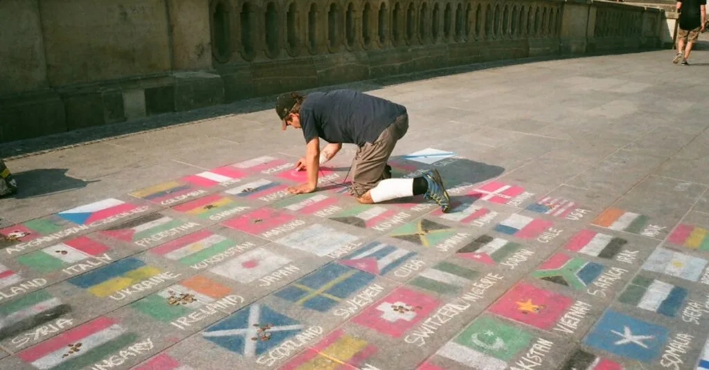 A street artist draws colorful flags with chalk on pavement, showcasing creativity and cultural diversity.