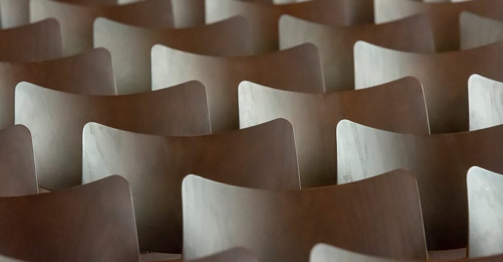 Symmetrical rows of wooden chairs creating a rhythmic and abstract pattern indoors.