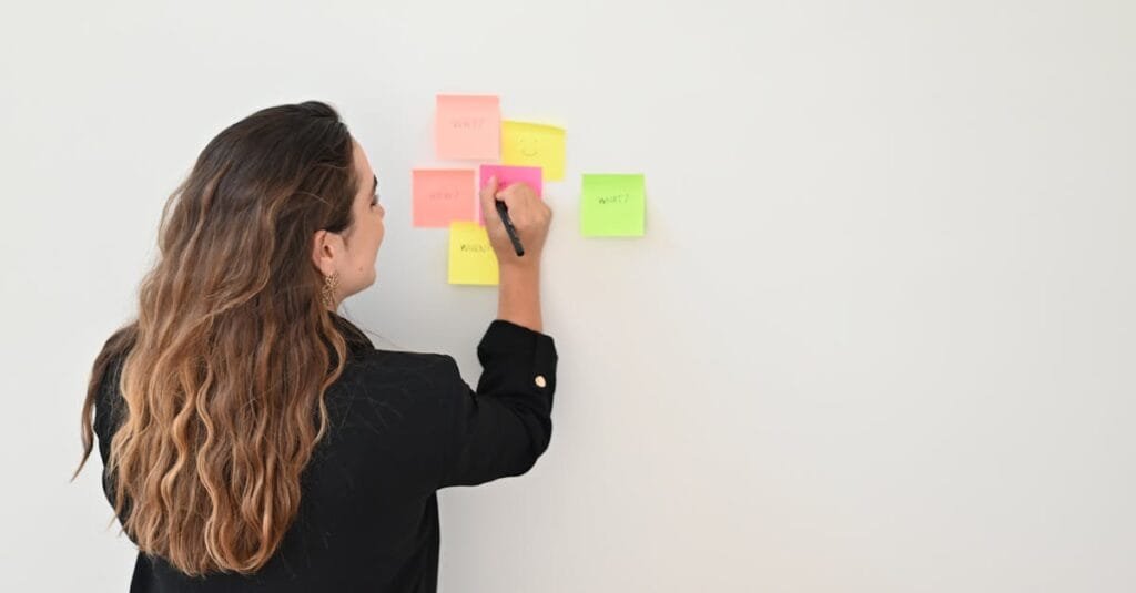 A businesswoman writes on colorful sticky notes on a white wall in an office setting.