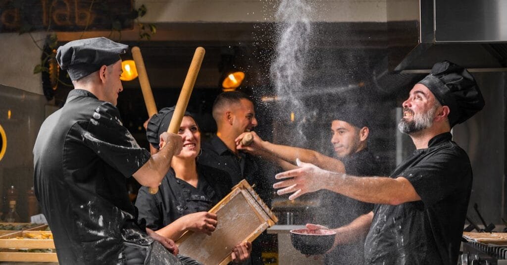 Lively group of chefs in black uniforms making pasta in a restaurant kitchen.