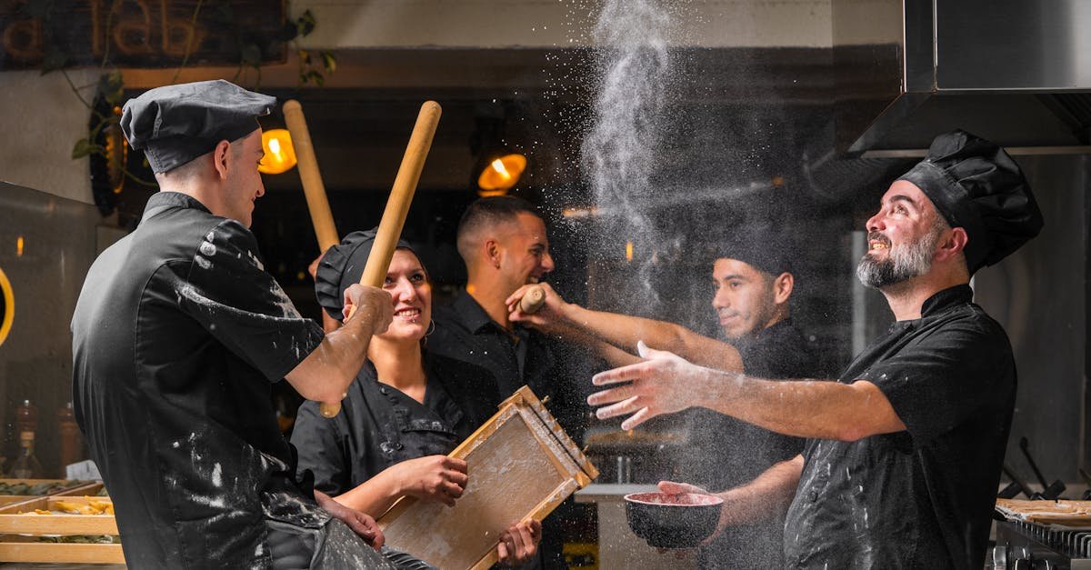 Lively group of chefs in black uniforms making pasta in a restaurant kitchen.