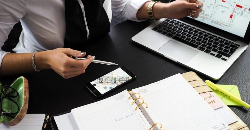 A business professional working on real estate project plans using multiple devices in an office setting.