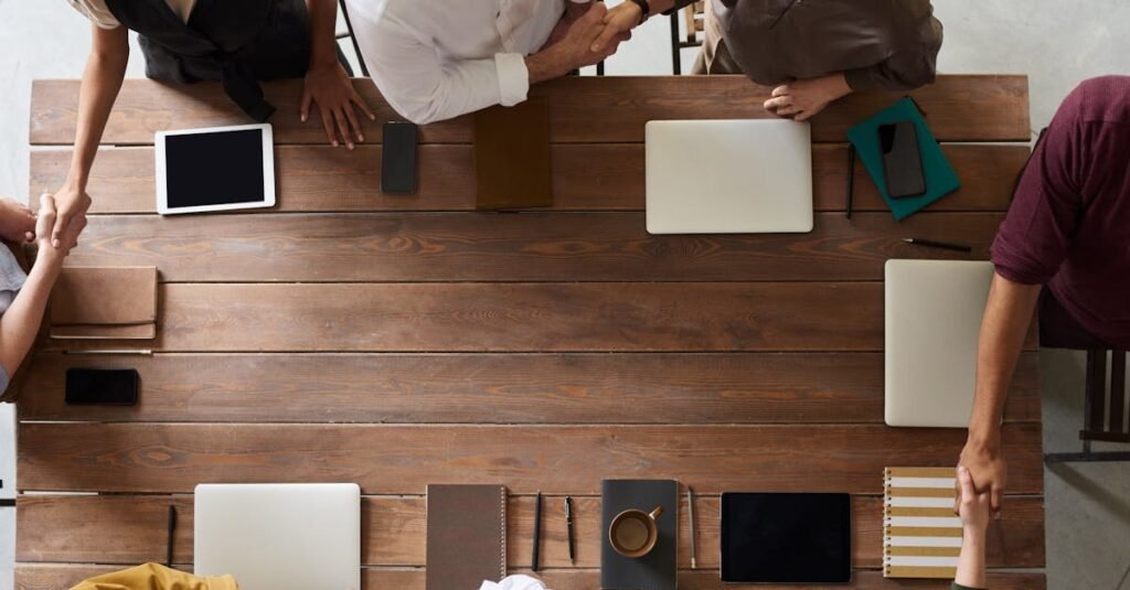 Group of adults having a business meeting, discussing plans around a wooden table with tech devices.