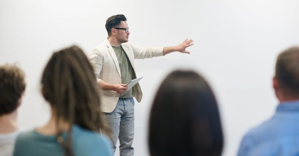 A man in a blazer gives a presentation to a captivated audience in a lecture setting.