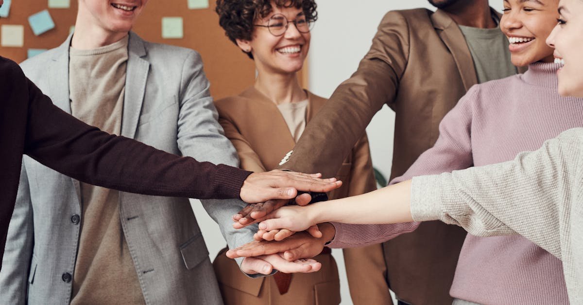 A group of happy, diverse colleagues celebrating teamwork and cooperation with a group high five indoors.