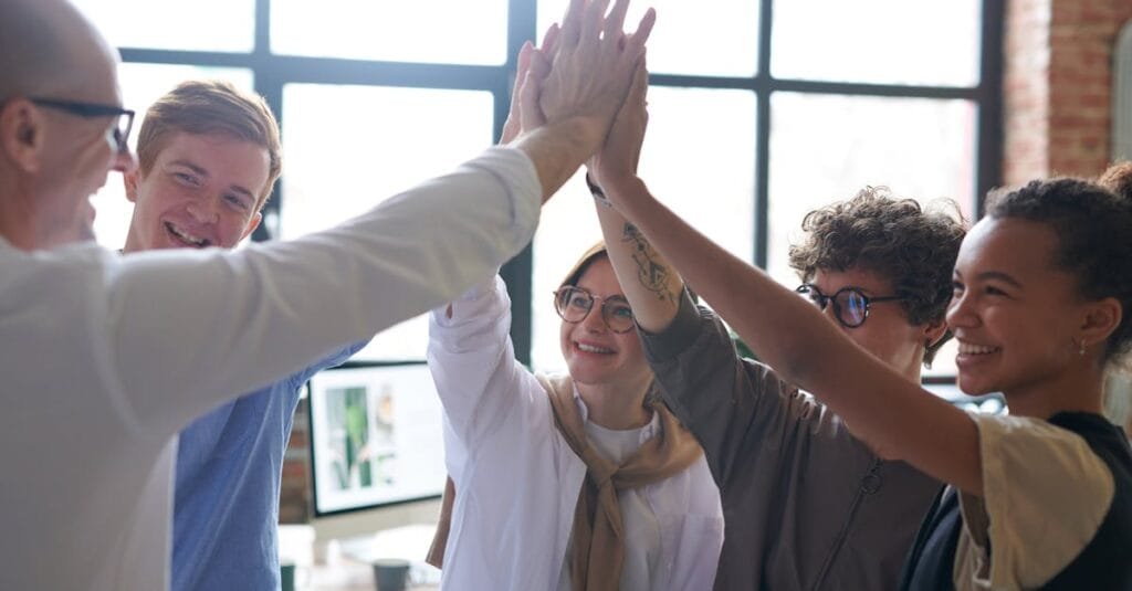 A diverse team of professionals celebrating success with a high five in a modern office.