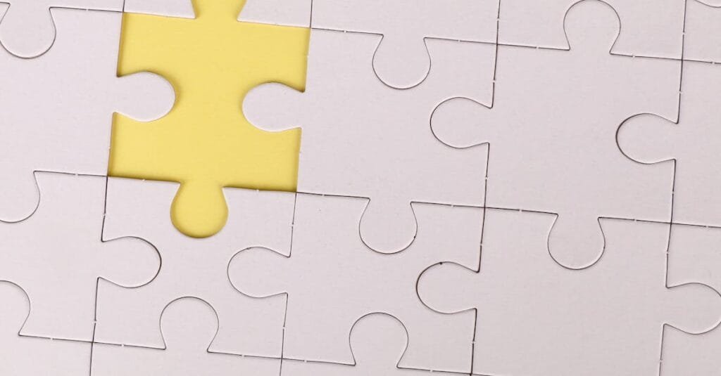 Close-up of a white jigsaw puzzle with a single yellow piece missing, symbolizing incompleteness.