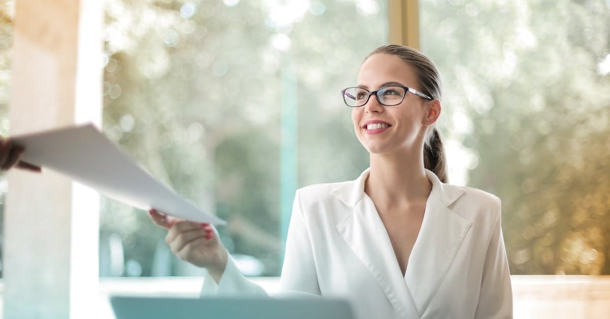 Low angle of successful female executive manager in classy style sitting at table with laptop in contemporary workplace and passing documents to colleague