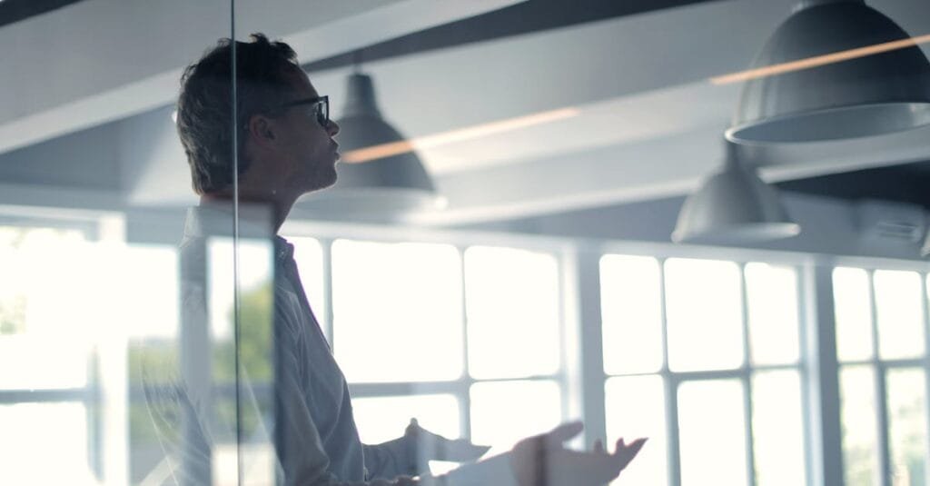 Business professional giving a presentation in a modern office setting through glass.