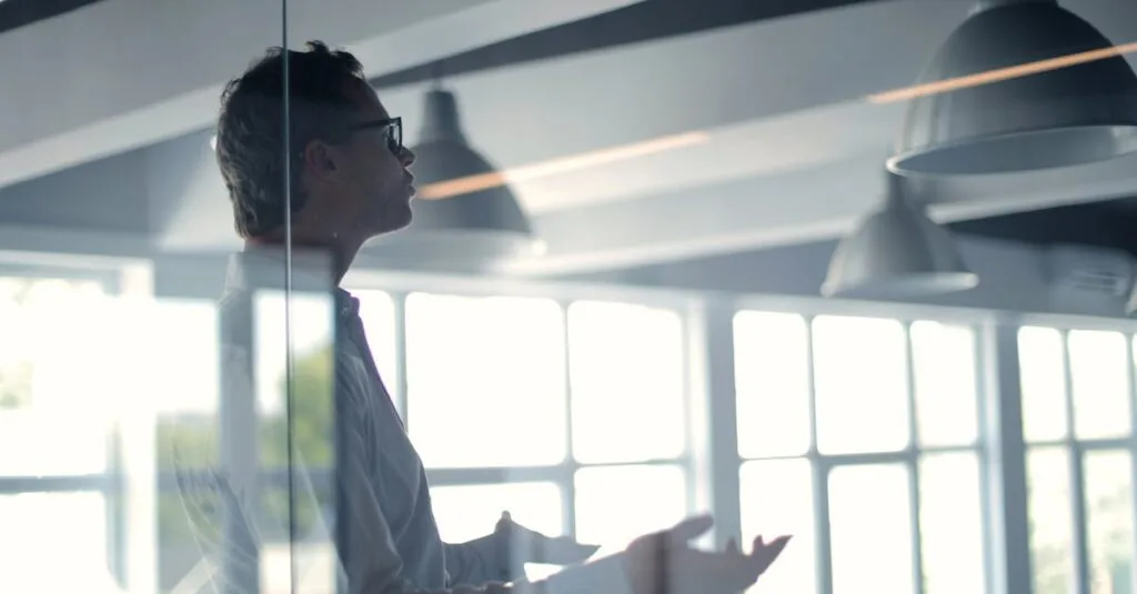 Business professional giving a presentation in a modern office setting through glass.