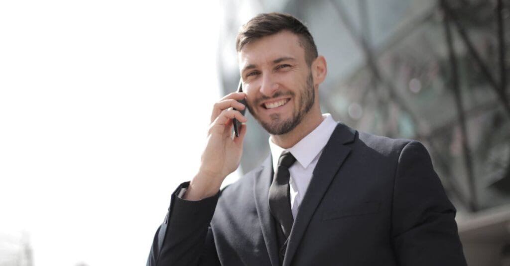 Smiling businessman in a suit having a phone call outside a modern glass building.