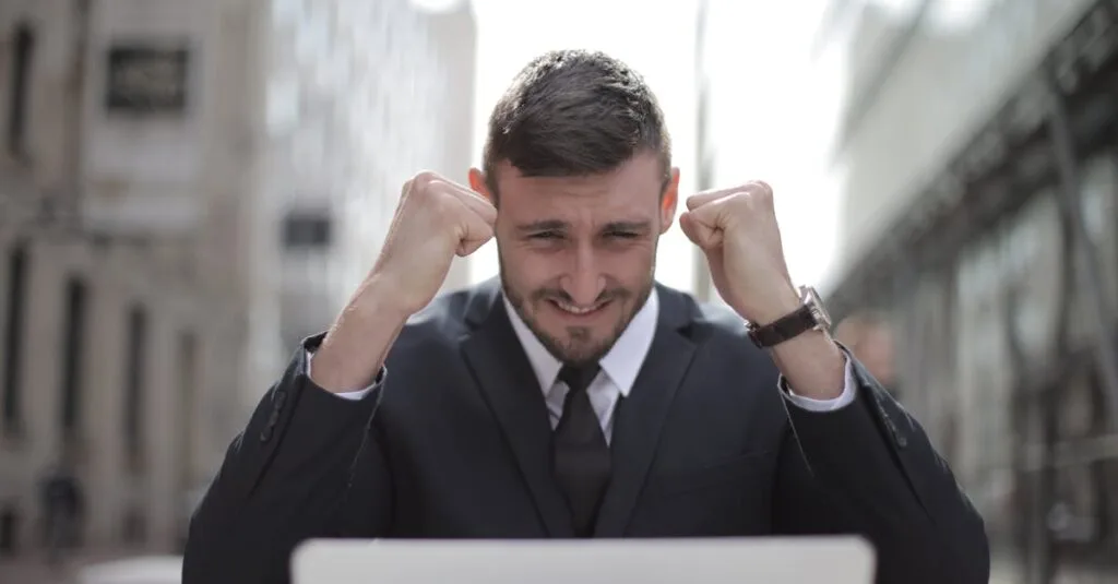 A joyful businessman in a suit triumphantly celebrates success on his laptop outdoors.