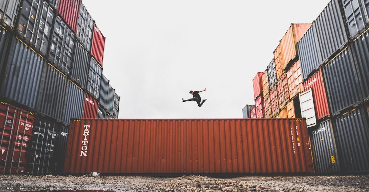 A person leaps dramatically above stacked shipping containers, showcasing freedom and industrial energy.