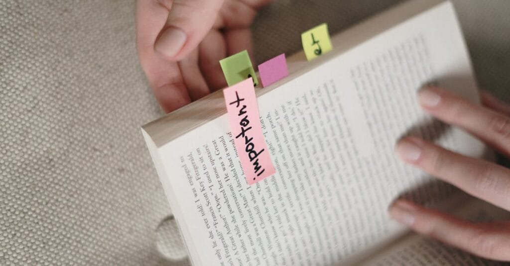 Hands holding a book with colorful sticky notes marking important pages.