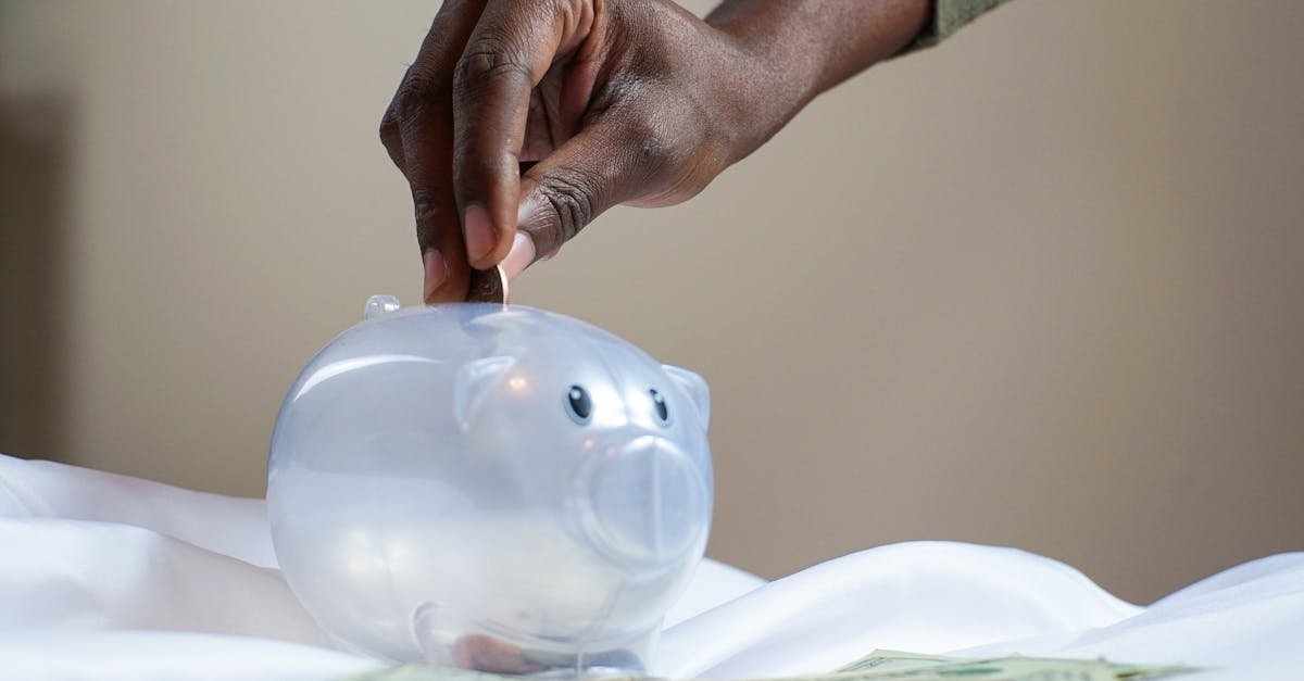 Close-up of a person's hand placing coins into a transparent piggy bank to save money.