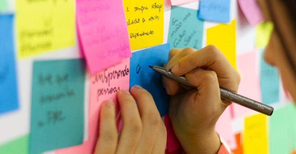 Hands writing on colorful sticky notes during a brainstorming session indoors.
