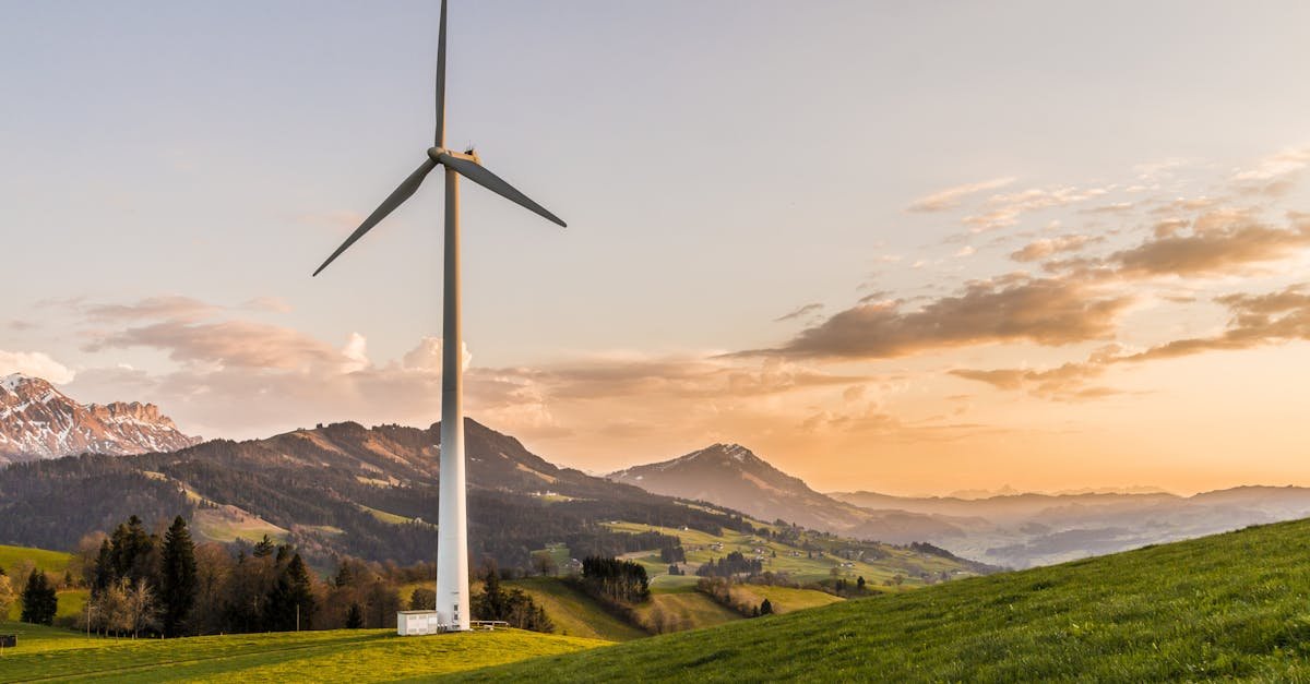 Wind turbine amid rolling hills and mountains at sunset, symbolizing renewable energy and sustainability.