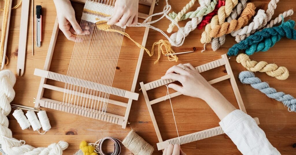 Hands weave yarn on looms in a vibrant workshop, showcasing creative craftsmanship with colorful threads.