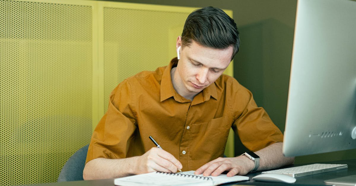 A man concentrating on his studies, taking notes at a desk with a computer.