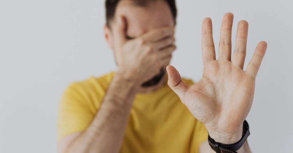 Close-up of a man covering his face and showing a stop gesture with his hand.