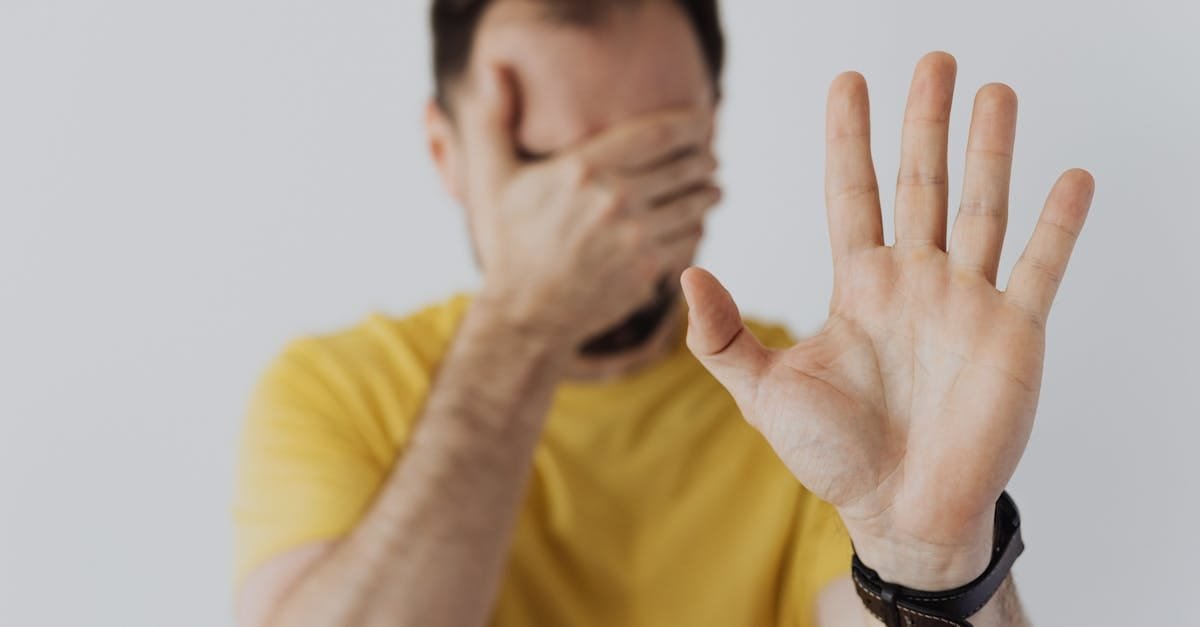 Close-up of a man covering his face and showing a stop gesture with his hand.