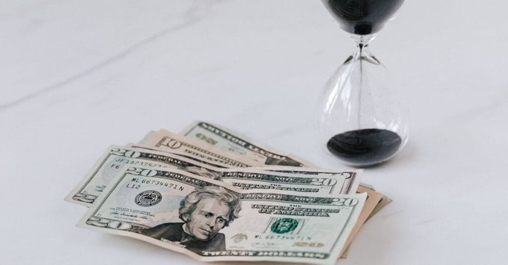 Close-up of US dollar bills with an hourglass, symbolizing time and money.