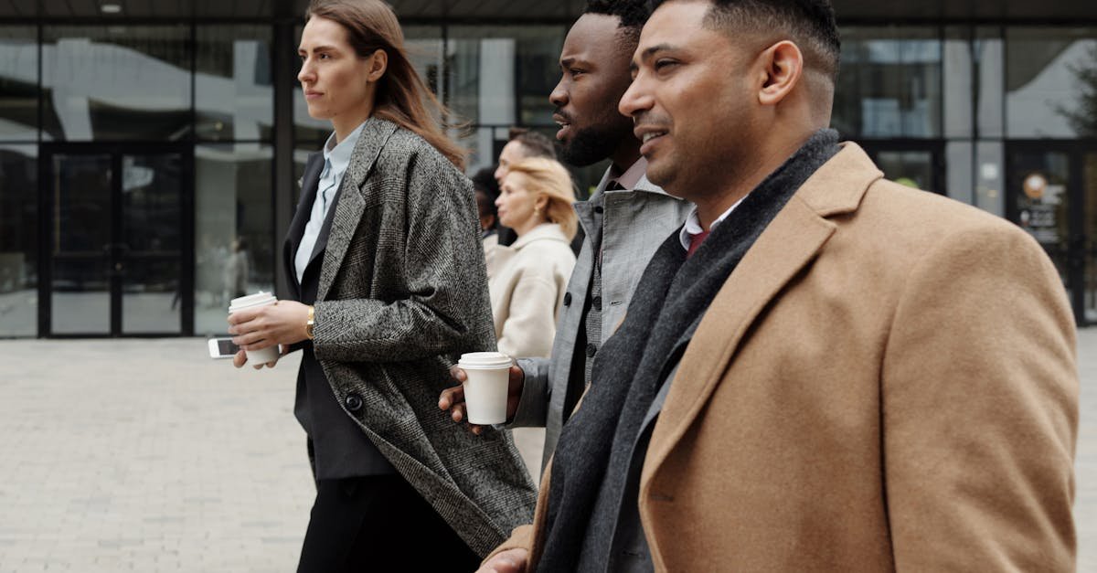 A diverse group of business professionals walking outside, holding coffee cups and discussing work.