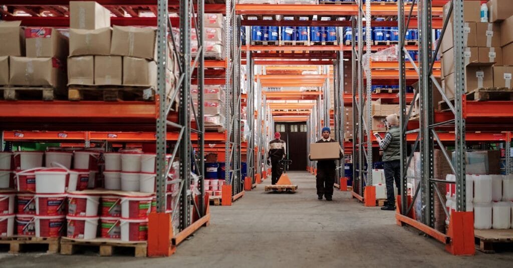 Warehouse interior showing workers handling boxes and organized shelves filled with products.