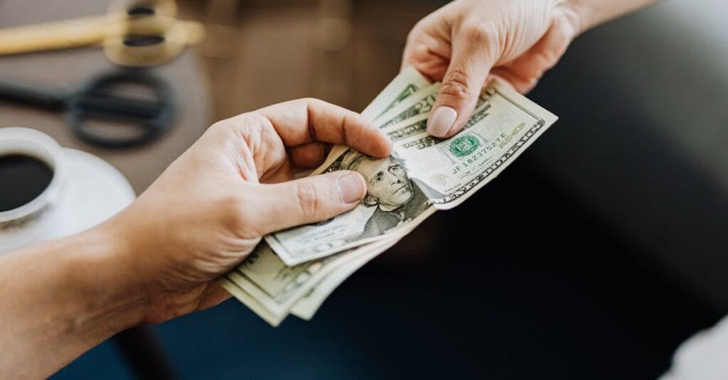 A close-up image of hands exchanging US dollar bills, symbolizing financial transaction or payment.