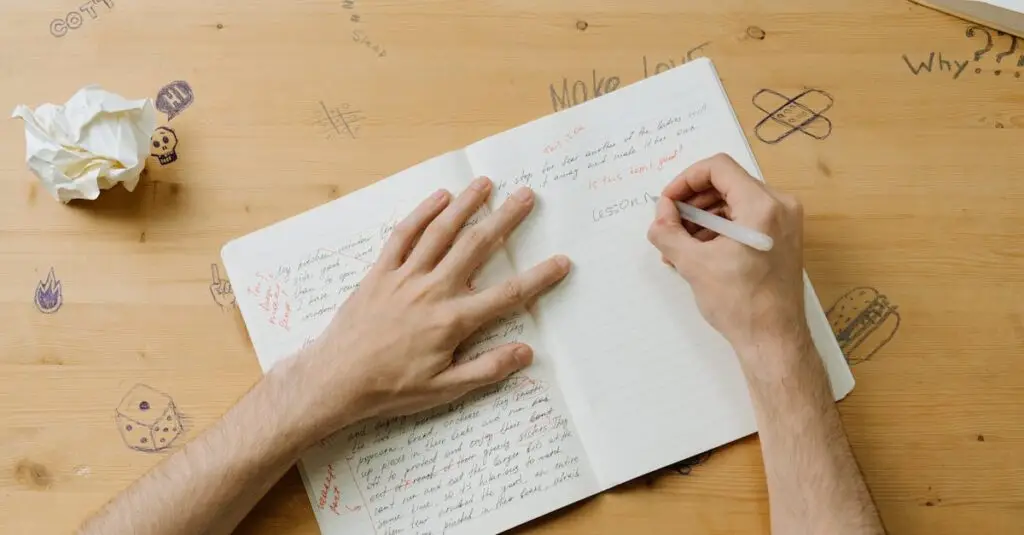 A person writing notes on a notebook with doodles on a wooden desk, reflecting creativity and education.