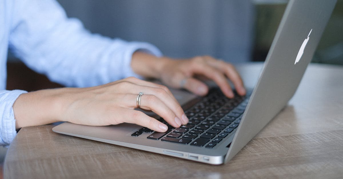 Crop faceless female entrepreneur wearing casual clothes sitting at wooden desk and browsing portable netbook in daylight