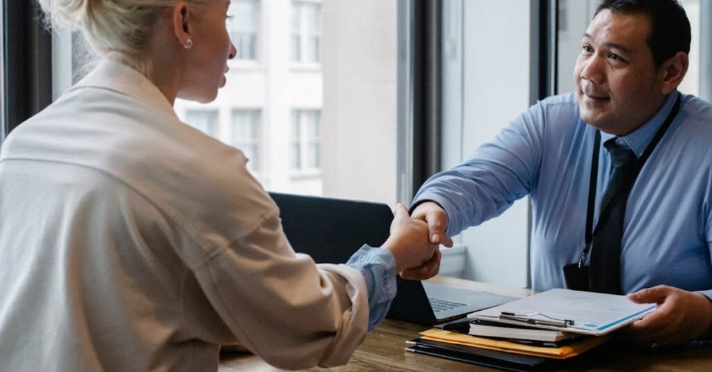Two professionals in an office setting shaking hands after a business agreement.
