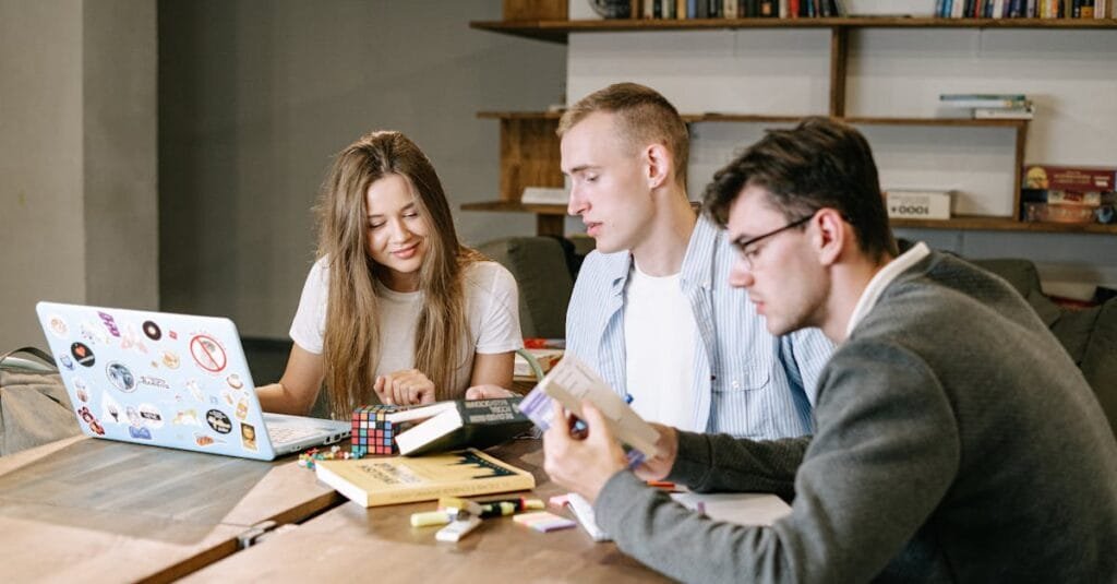A group of young professionals collaborating on a project in a modern office space, working with books and a laptop.