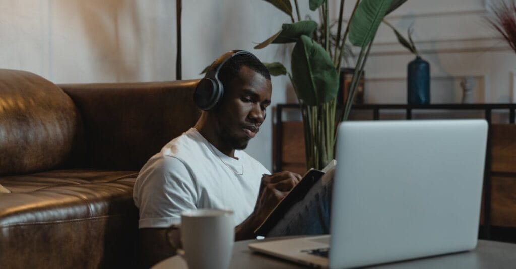 African American man wearing headphones, engaged in online learning at home with a laptop.