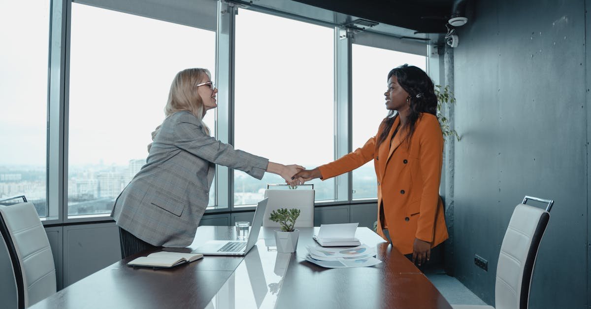 Two businesswomen shaking hands in a modern office setting, symbolizing partnership and agreement.