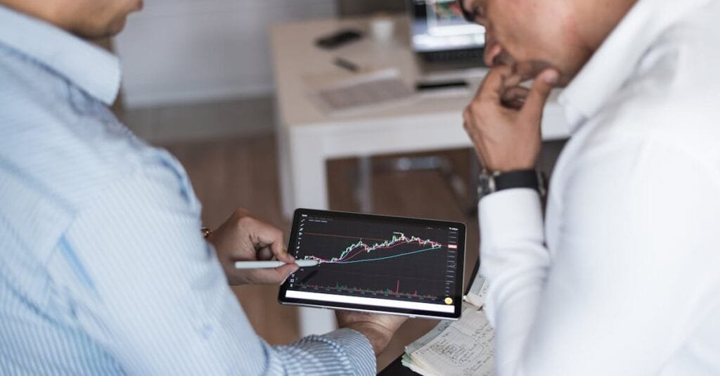 Two businessmen using a tablet for online trading analysis in an office setting.