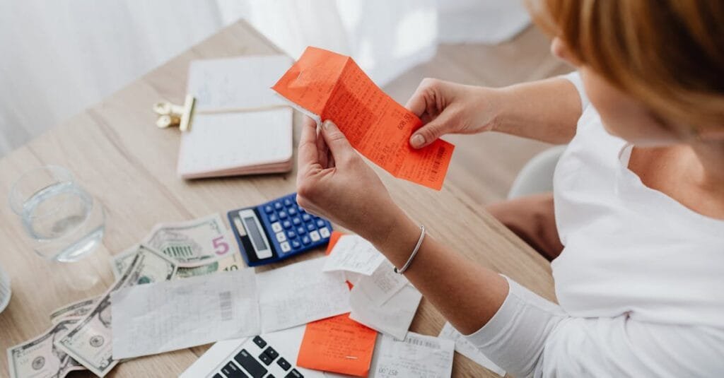 Woman using calculator and receipts at home office desk for finance management.