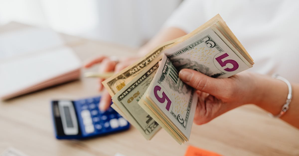 Close-up of hands counting US dollar bills with a calculator, highlighting finance and savings.