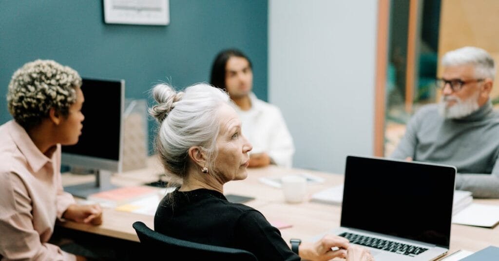 A multicultural team engaged in a meeting around a conference table with laptops.