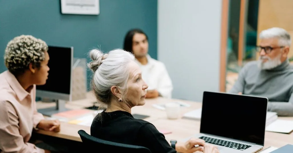 A multicultural team engaged in a meeting around a conference table with laptops.