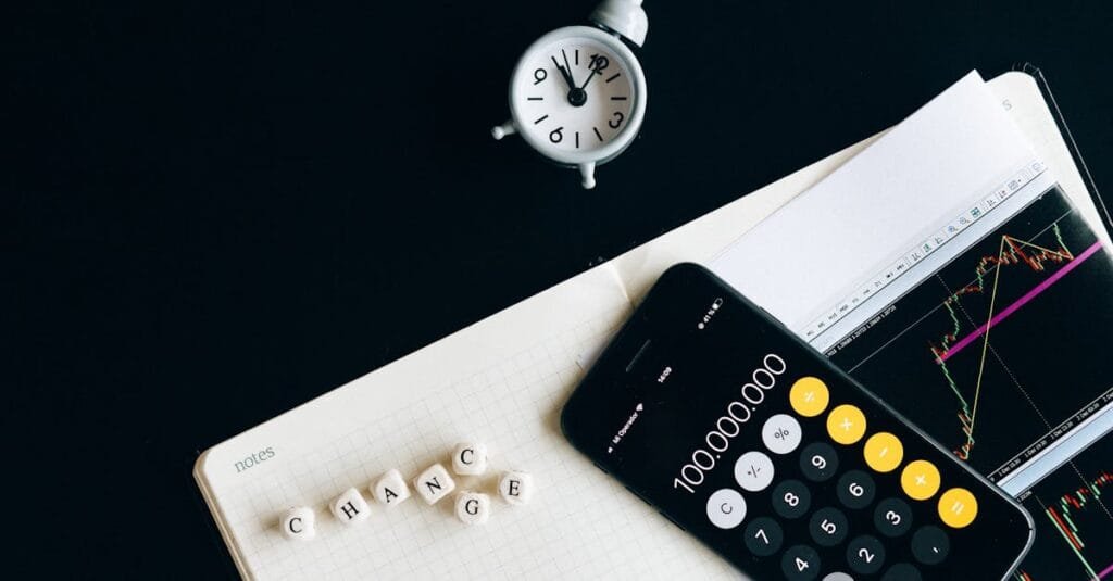 Notebook with an iPhone displaying 100,000,000, desk clock and financial charts suggesting market analysis.