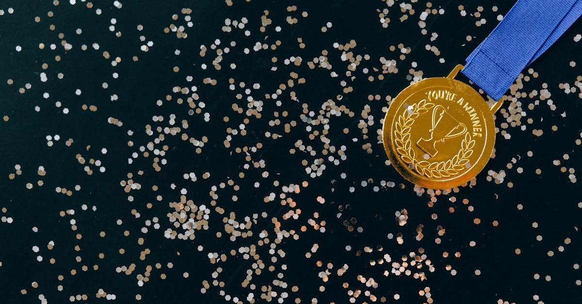Close-up of a gold medal with blue ribbon and confetti on a black surface, symbolizing victory.