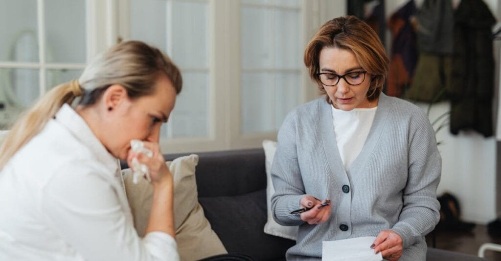 A counseling session with two women discussing important matters on a comfortable sofa indoors.