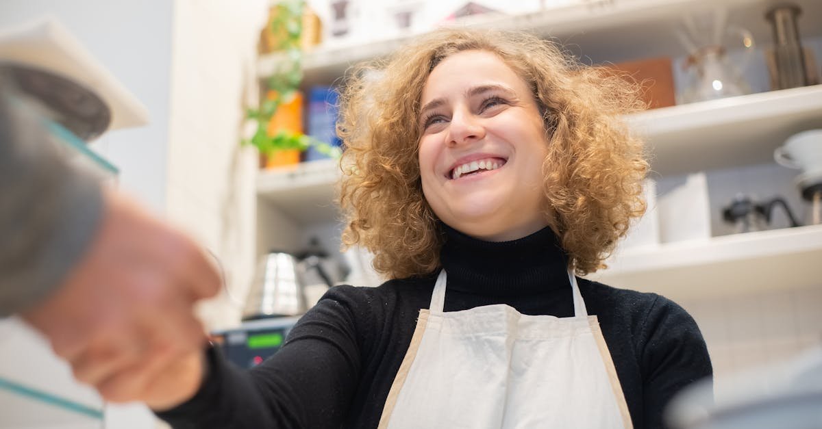Smiling barista in café, engaging positively with customer, signifying hospitality.