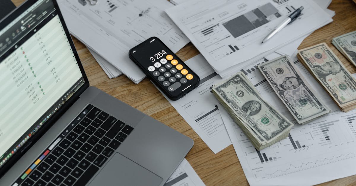 A desk with financial documents, currency, a laptop, and phone calculator.