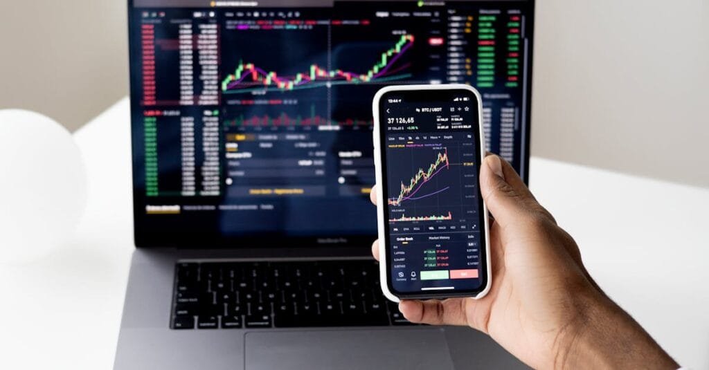 Person checking stock market graphs on laptop and smartphone, focusing on financial data.