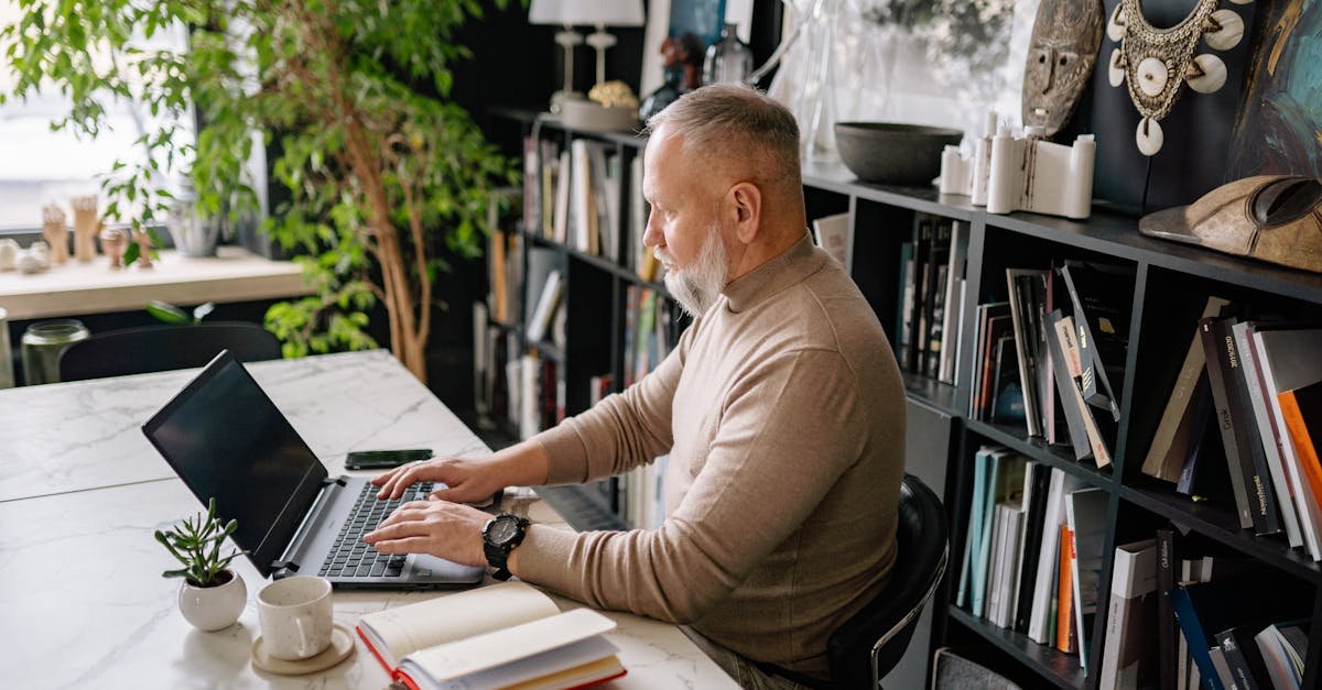 Senior man focused on laptop in a stylish home office, surrounded by books and plants.