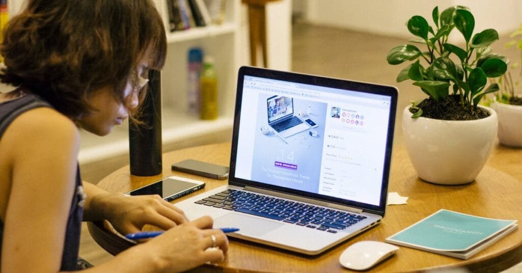 Woman working remotely from home with a laptop, pen, and plant on her desk, highlighting digital nomad lifestyle.