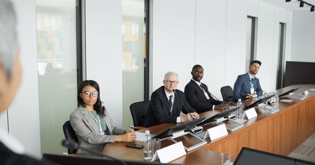 A diverse group of professionals in a modern office setting, seated around a conference table during a business meeting.