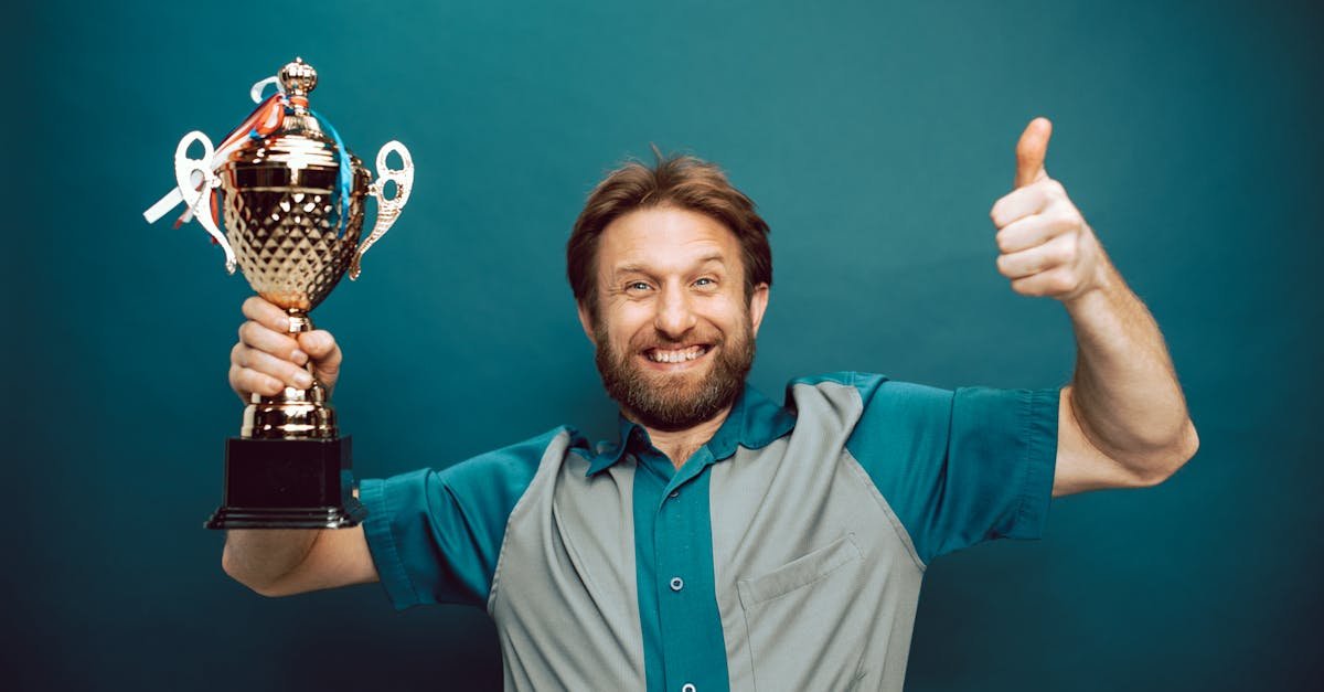 Smiling man holding a trophy and giving a thumbs up gesture against a blue backdrop.